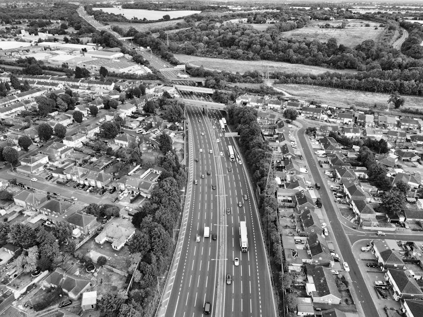 A black-and-white aerial photograph of Devons Road in Bow showing a busy multi-lane road with various vehicles including cars, vans, and trucks traveling in both directions. The road is flanked by res